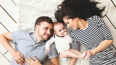 Family Consumer Loans - couple with baby laying on floor smiling at each other.