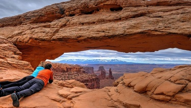 Friends enjoying the sweeping view through Mesa Arch in Utah's Canyonlands National Park