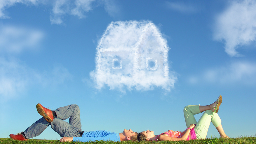A couple lies on the grass while a house-shaped cloud floats above them