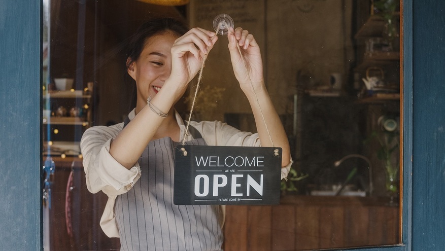 A female business owner puts an open sign on the front door of her shop