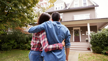 A couple stands outside looking at the front door of their newly purchased home