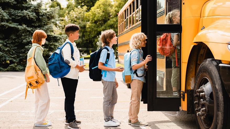 A group of elementary school children line up to get on the bus