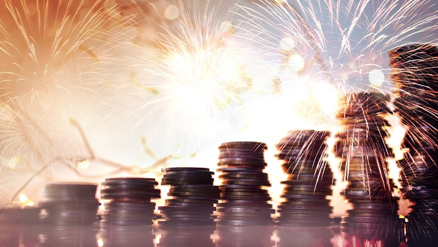 A row of stacked coins are lit up by a background of sparkler fireworks