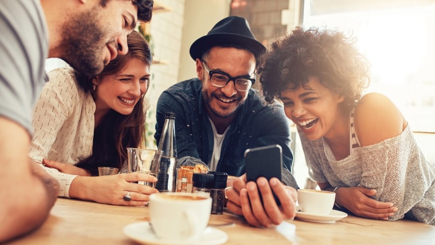 A group of young friends look at their mobile phone while having drinks at a coffee shop