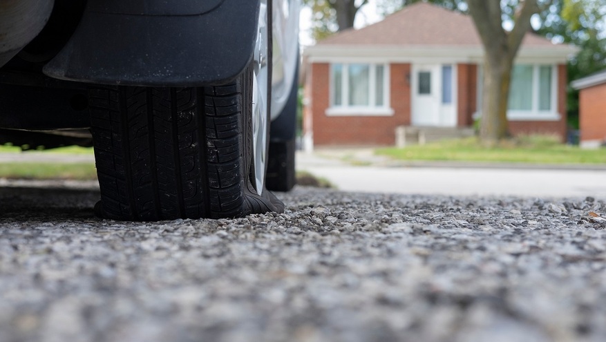 A car with a flat tire sits outside a home