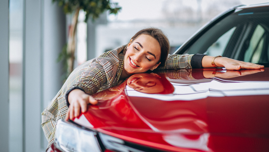 Smiling woman hugging a shiny red car in a showroom	