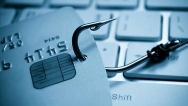 Phishing Attacks - close up of fishing hook in credit card on top of keyboard.