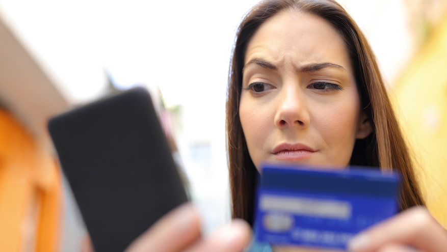 Suspicious woman looking at phone holding credit card.
