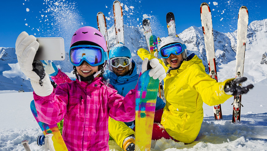 A family of three on the ski slopes smiles while a young girl takes a group selfie